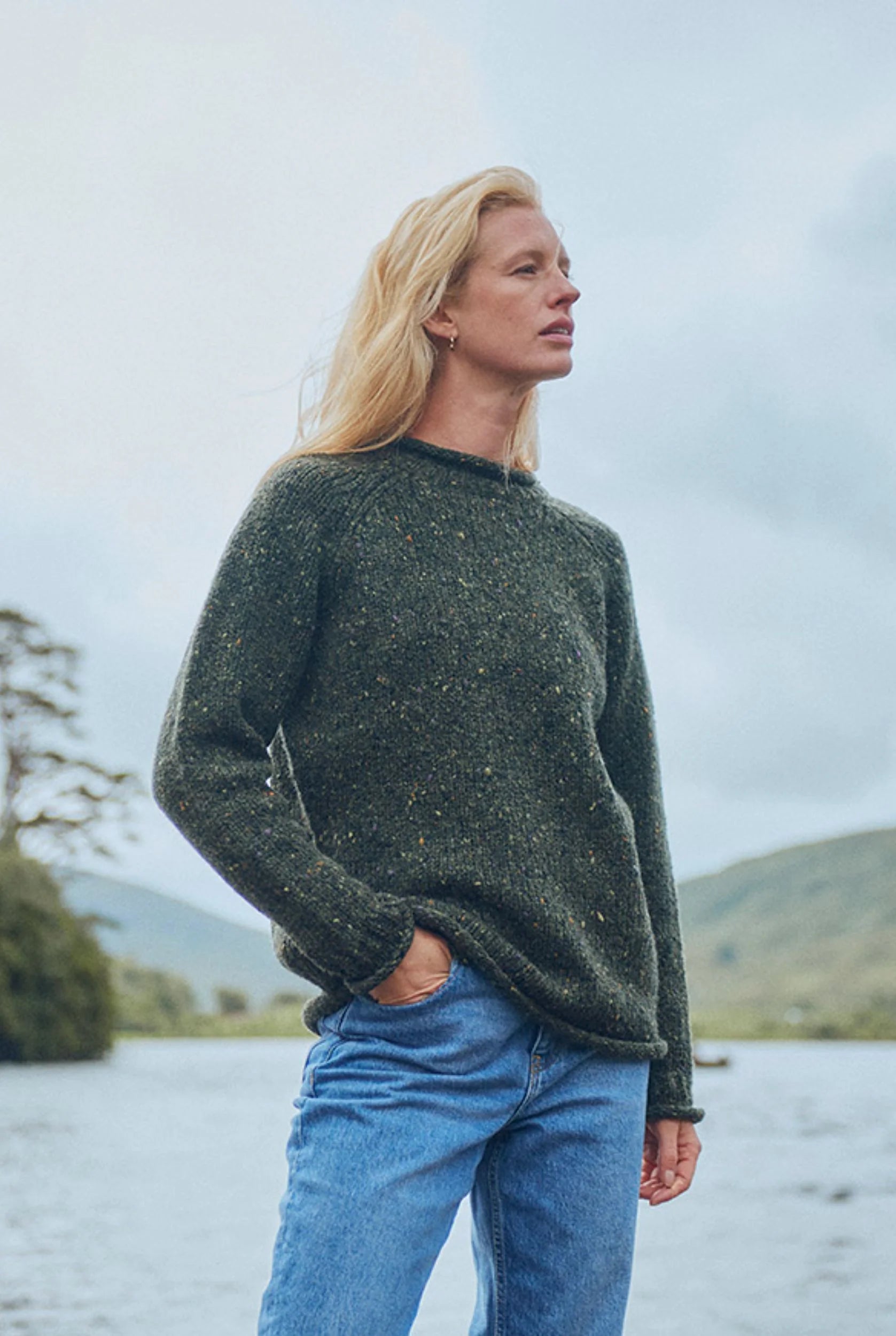 Brackloon Tweed Roll Neck Aran Sweater in deep forest green, styled by the water, 100% Donegal tweed wool.