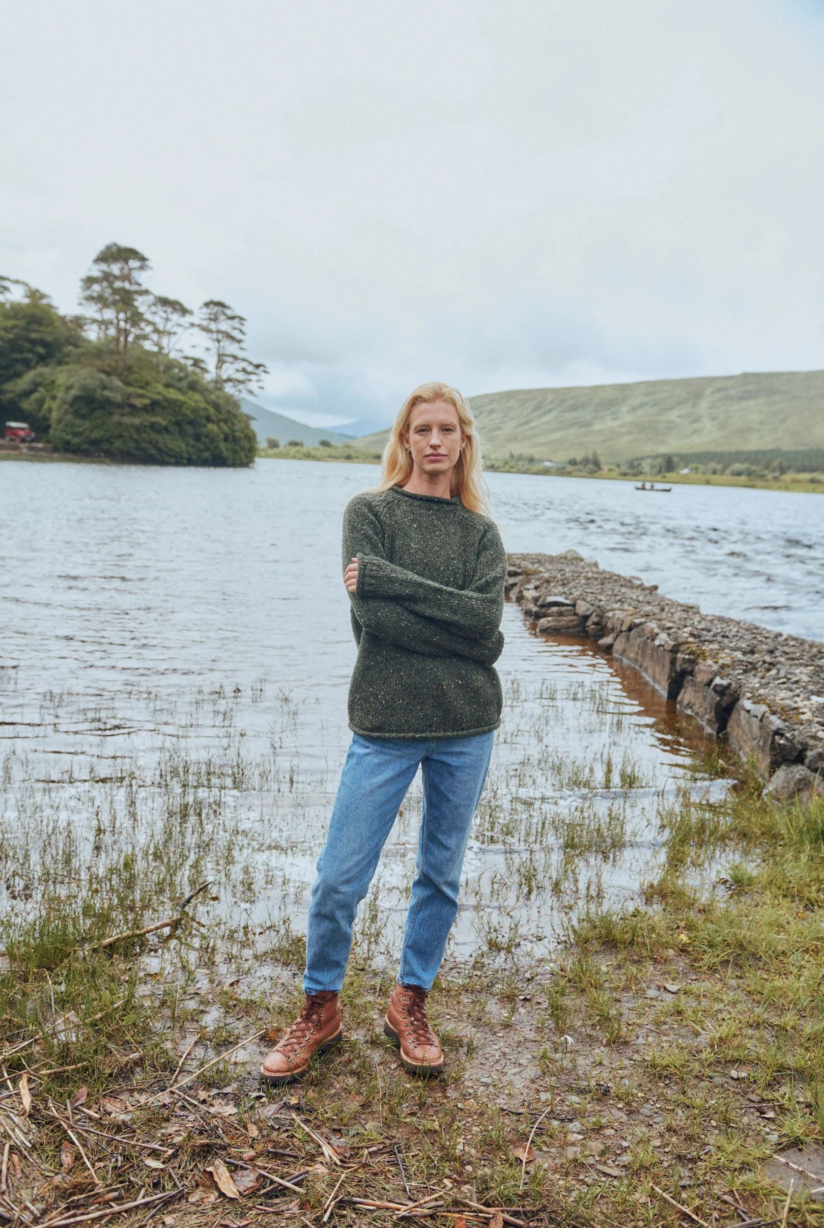 Model wearing Brackloon Tweed Roll Neck Aran Sweater in forest green, smiling, relaxed casual style.