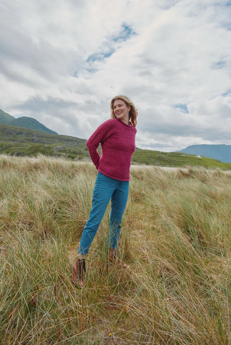 Brackloon Tweed Roll Neck Aran Sweater in pink heather, styled outdoors with jeans, 100% Donegal tweed wool.