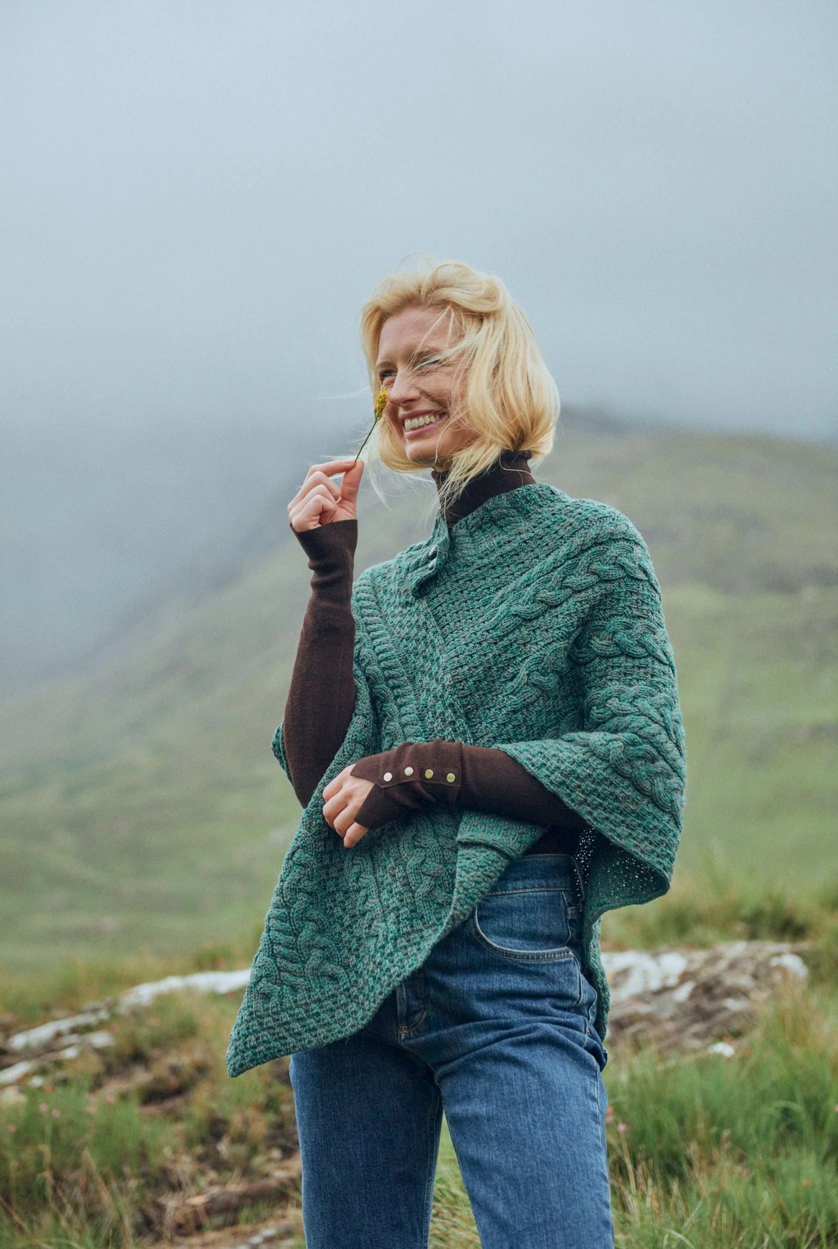Woman wearing a Connemara green merino wool poncho in a mountainous landscape.

