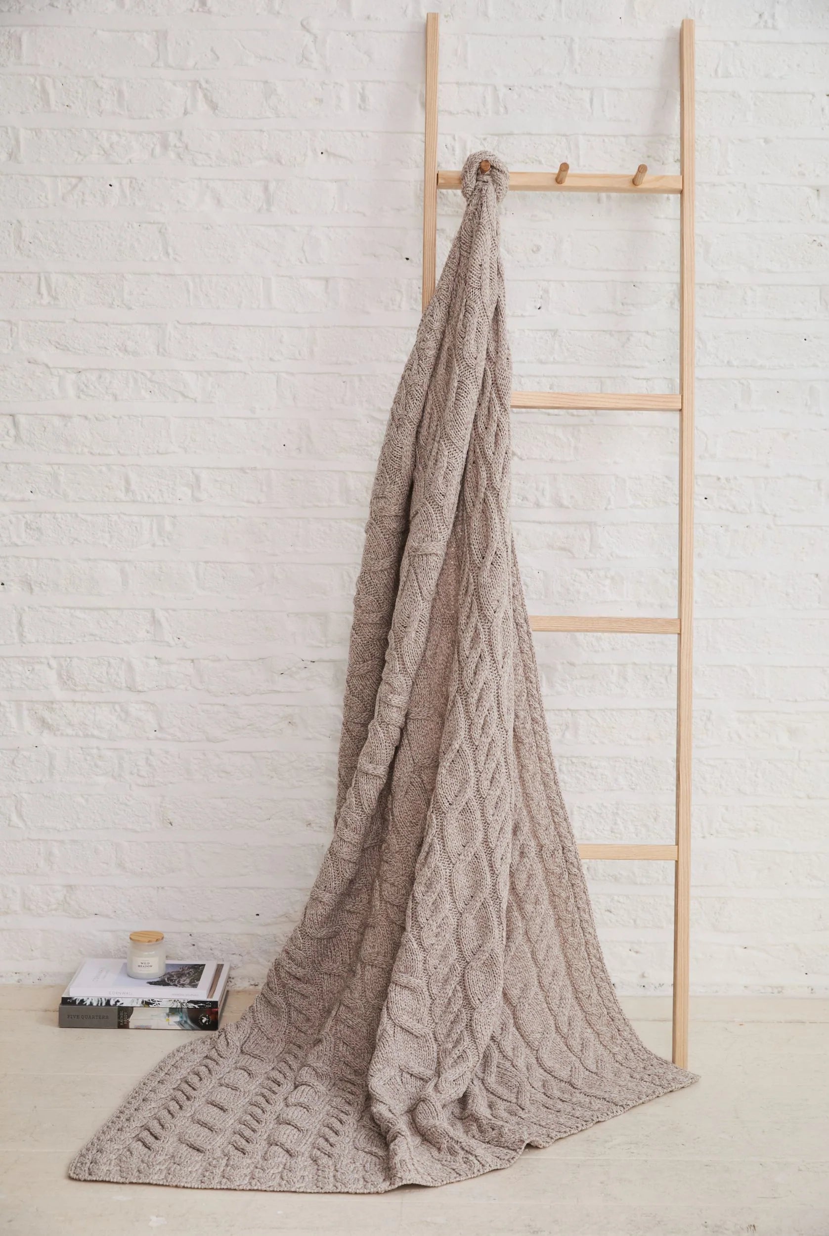 Silver Strand Supersoft Aran Cable Throw in Oat, draped over a woodden ladder showcasing traditional Aran knit patterns.
